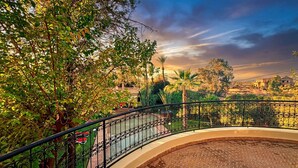A curved balcony with a wrought iron railing overlooking a landscaped garden with trees and a distant view of a town. - Charming Luxury Villa | Pool & Hot Tub (Marrakesh)