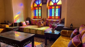 Ein Zimmer mit einer Sofagarnitur, einem Glastisch und zwei Buntglasfenstern.