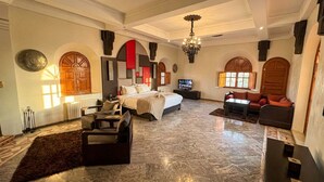 A spacious hotel room with a large bed, a television, a sofa, and a dining table. - Charming Luxury Villa | Pool & Hot Tub (Marrakesh)