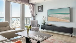 A modern living room with a large window, a sofa, a chair, a coffee table, and a TV on the wall. - High-Rise Sea-View Stay by Sea N' Rent (Tel Aviv)
