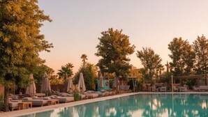 A poolside area with lounge chairs and umbrellas, surrounded by trees. - Waky Club | Designer Flat (Aghouatim)