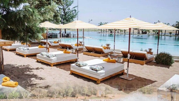 A poolside area with sun loungers and umbrellas, a wakeboarding area, and a view of the water. - Waky Club | Designer Flat (Aghouatim)