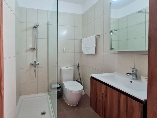 A modern bathroom with a glass shower enclosure, a white toilet, and a wooden vanity with a sink.