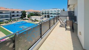 Un balcone con vista sulla piscina, arredi esterni e cielo sereno.
