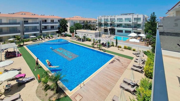 Un hotel con una grande piscina, lettini e vista sugli edifici circostanti.