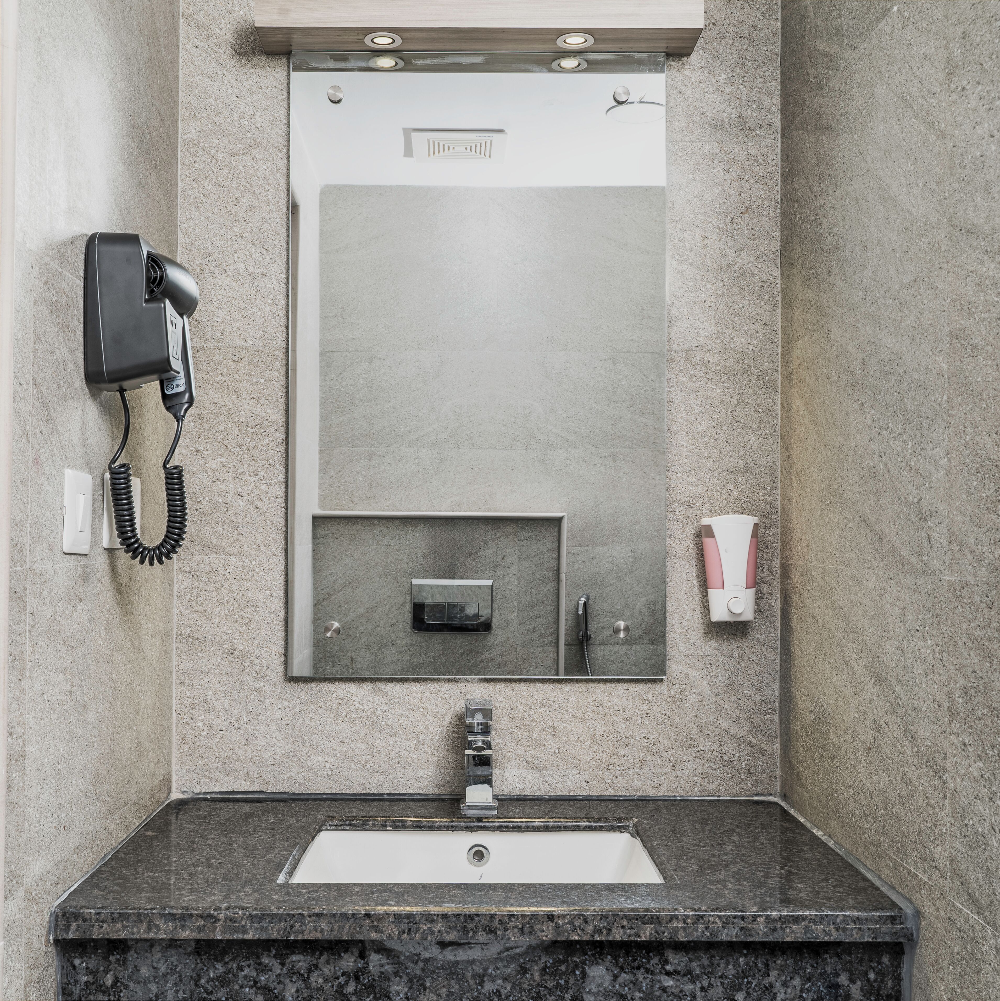A bathroom with a sink, mirror, hair dryer, and soap dispenser.