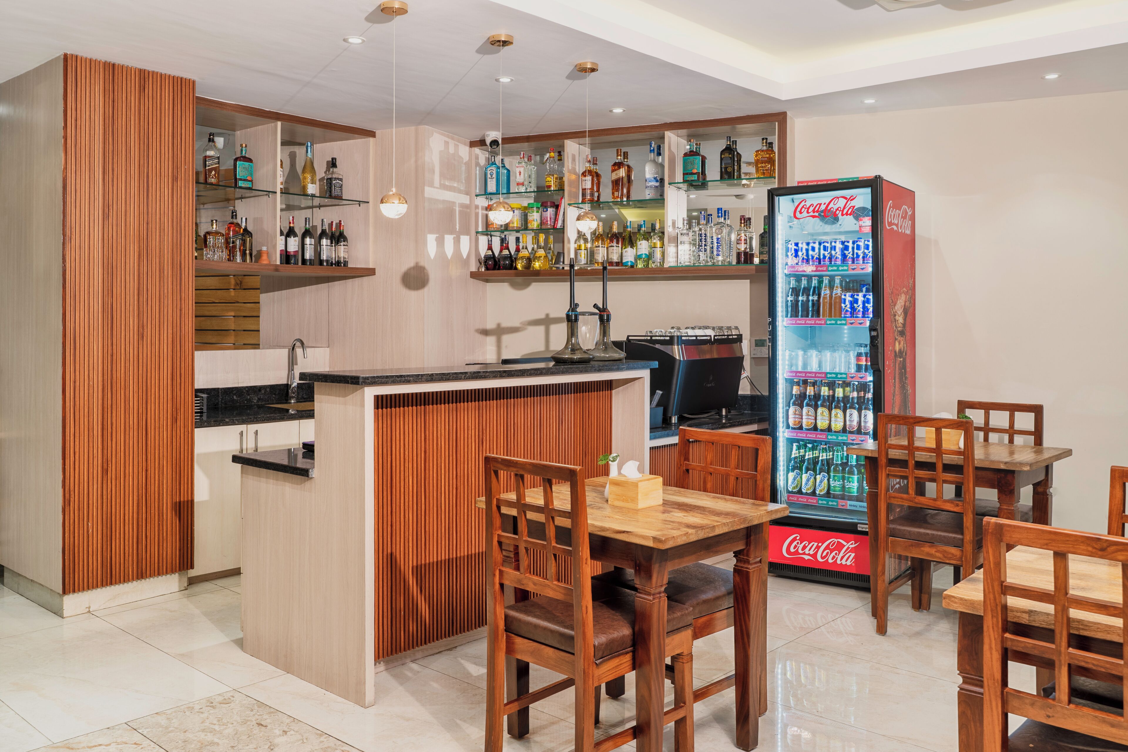 A bar area with a wooden bar counter, seating, and a Coca-Cola refrigerator.