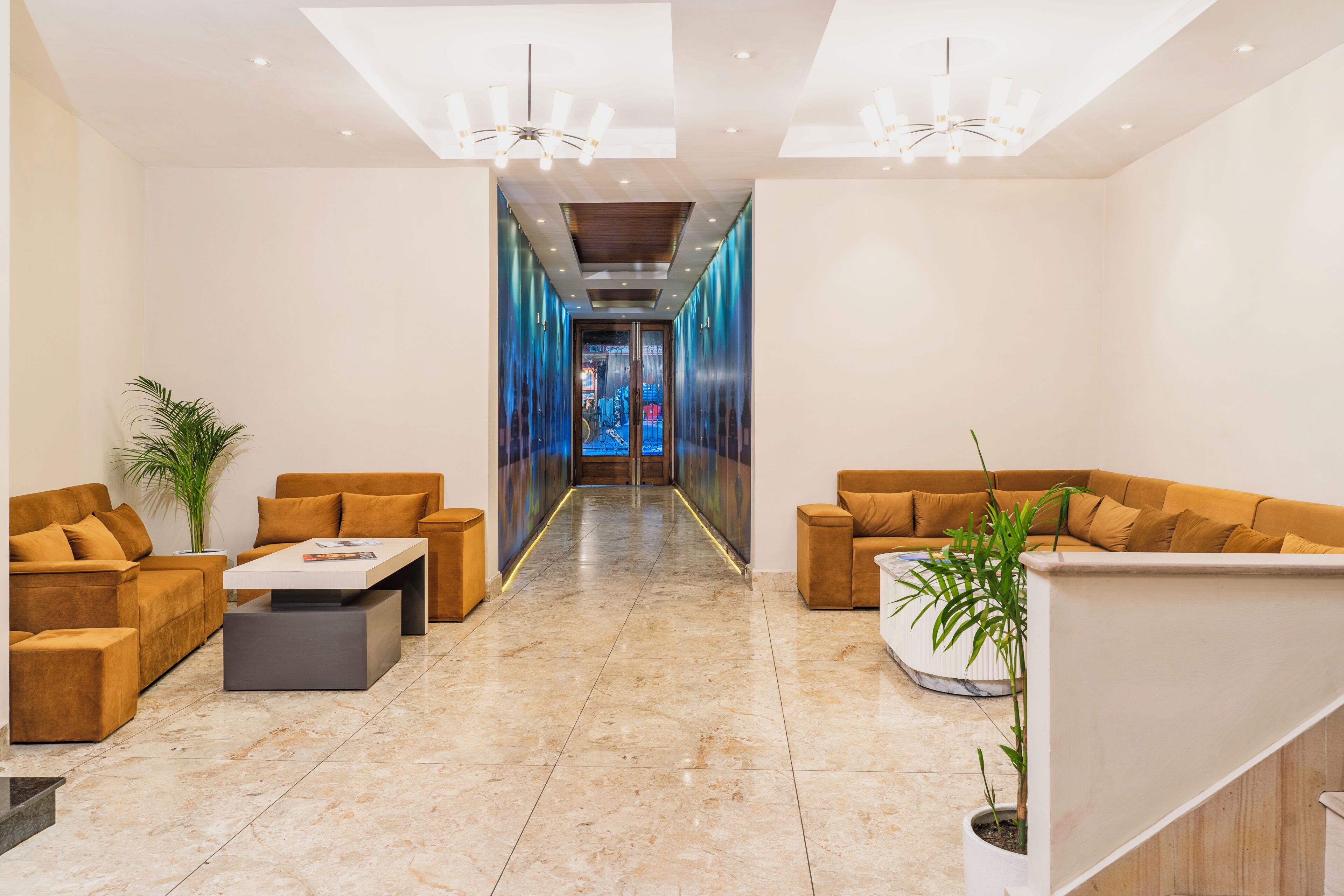 A hotel lobby with a central hallway, sofas, a reception desk, and a large window.