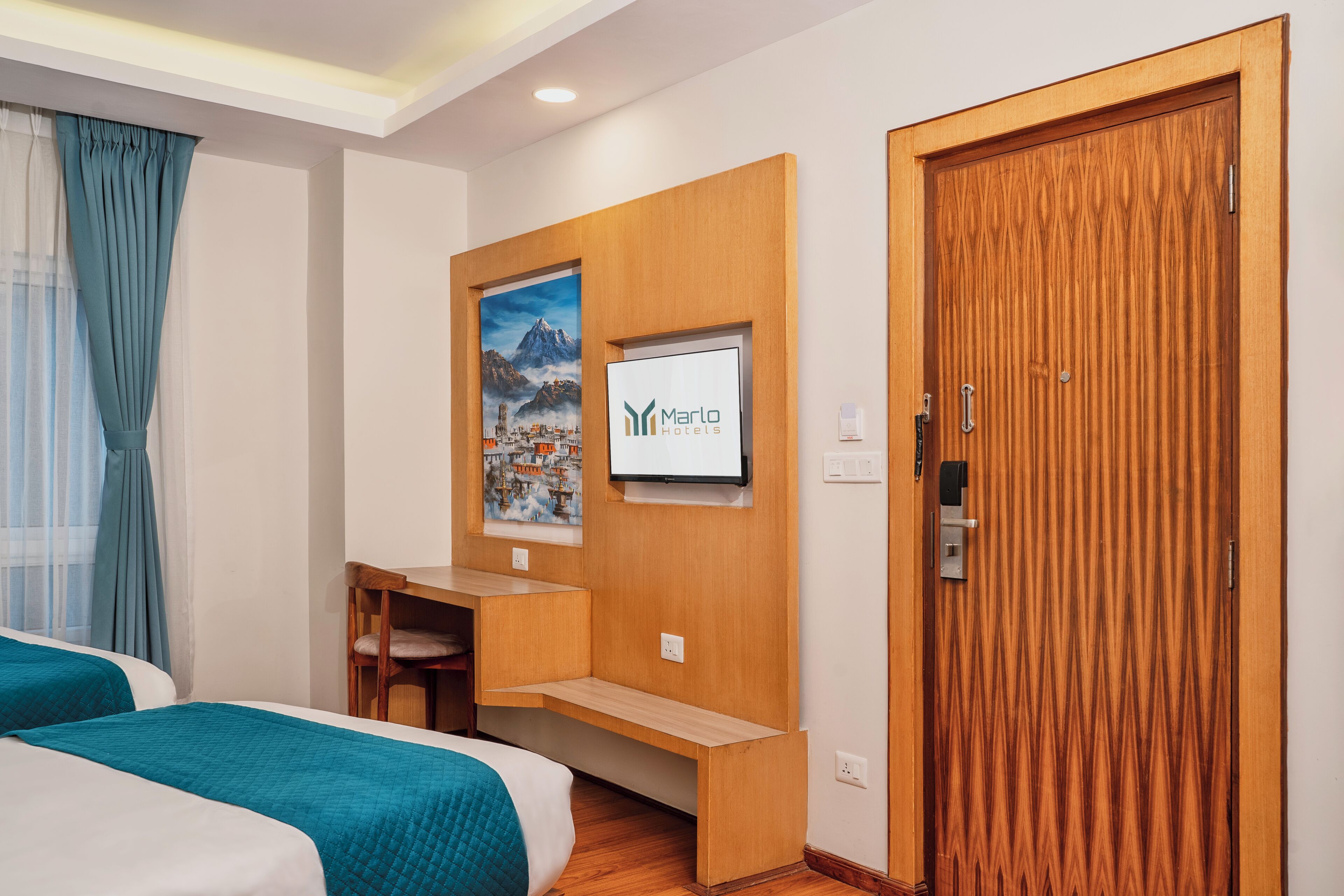 A hotel room with a bed, a desk, a TV mounted on the wall, and a wooden door.