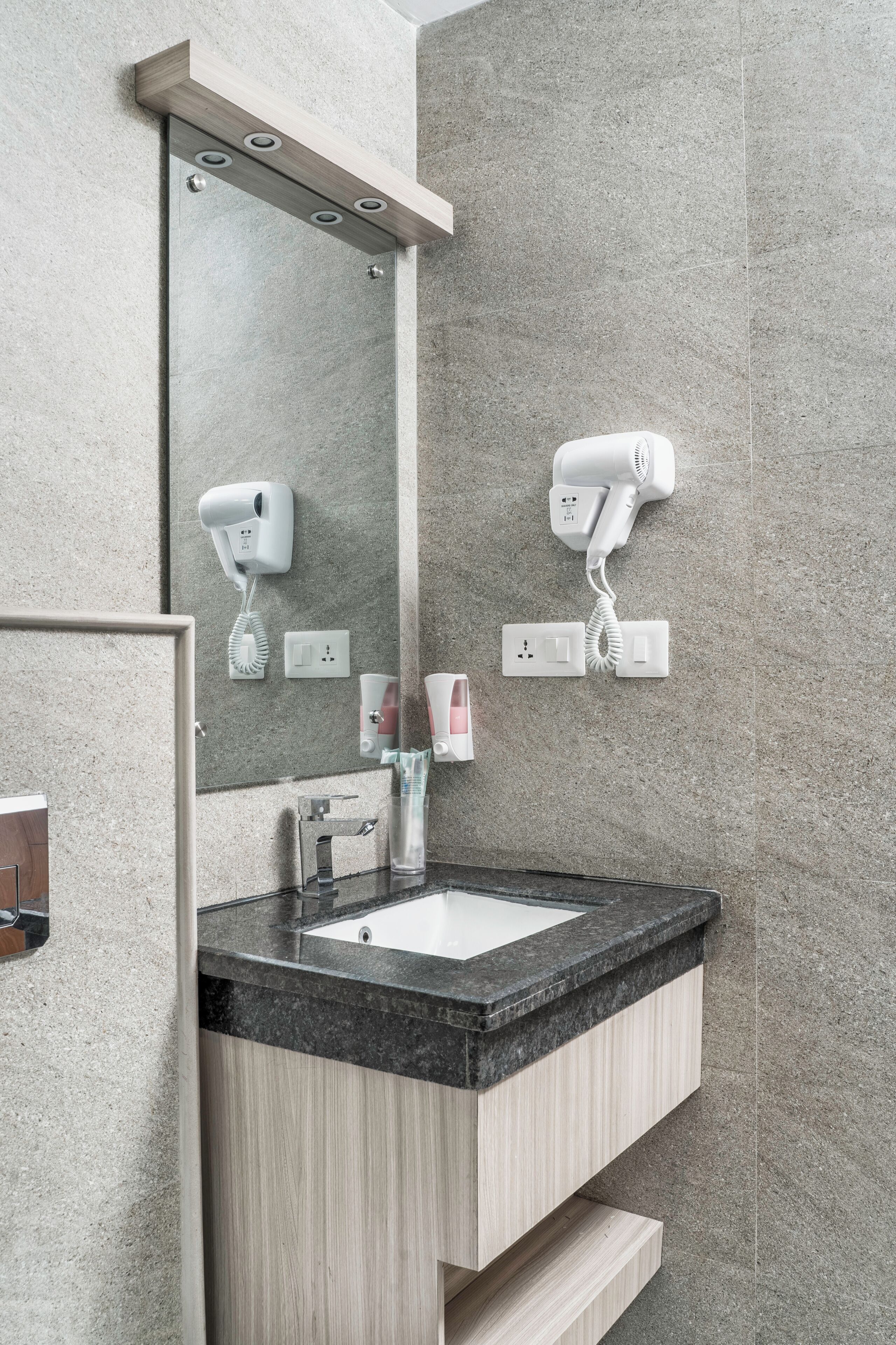 Un baño moderno con un espejo grande, un lavamanos y dos secadores de pelo fijos en la pared.