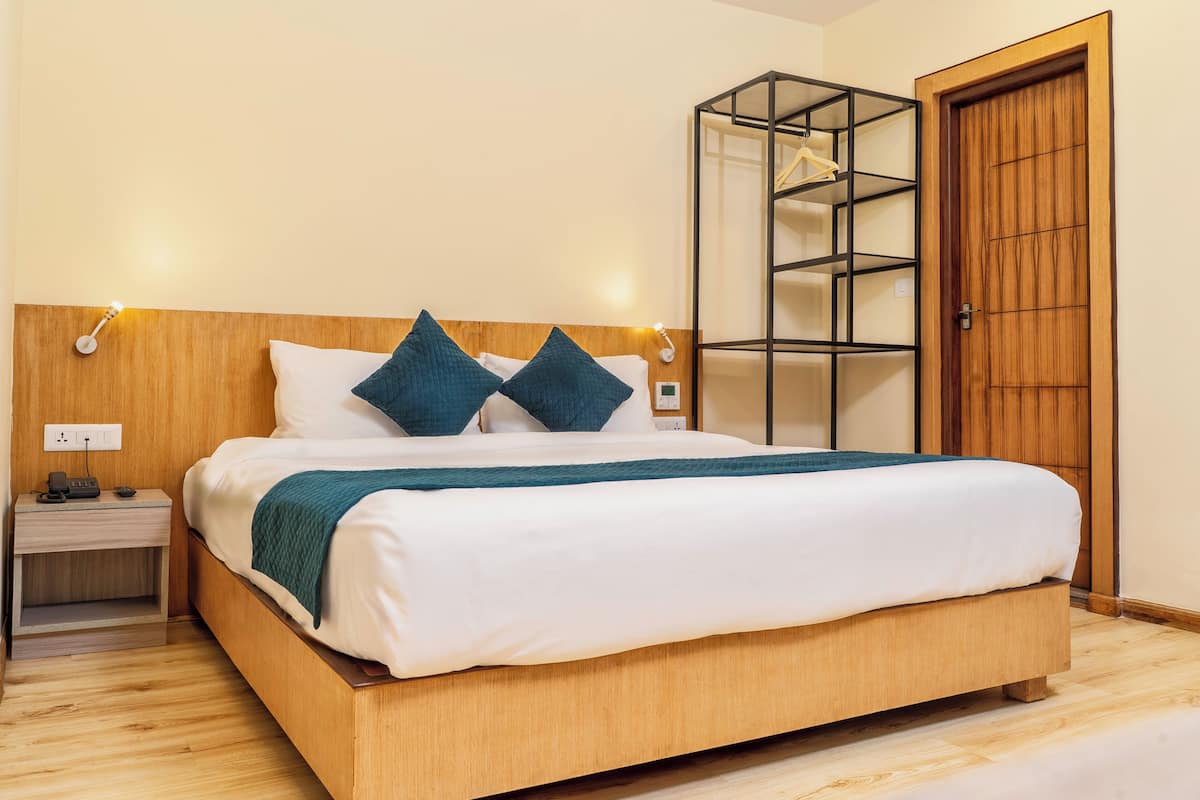 A neatly made bed with a wooden headboard, a bedside table with a phone and charger, and a wooden wardrobe with a mirrored door.