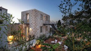Edificio de piedra con balcón, rodeado de plantas y una terraza de madera.