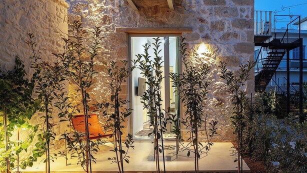 Un edificio de piedra con balcón, una puerta y un pequeño jardín con plantas y un banco.