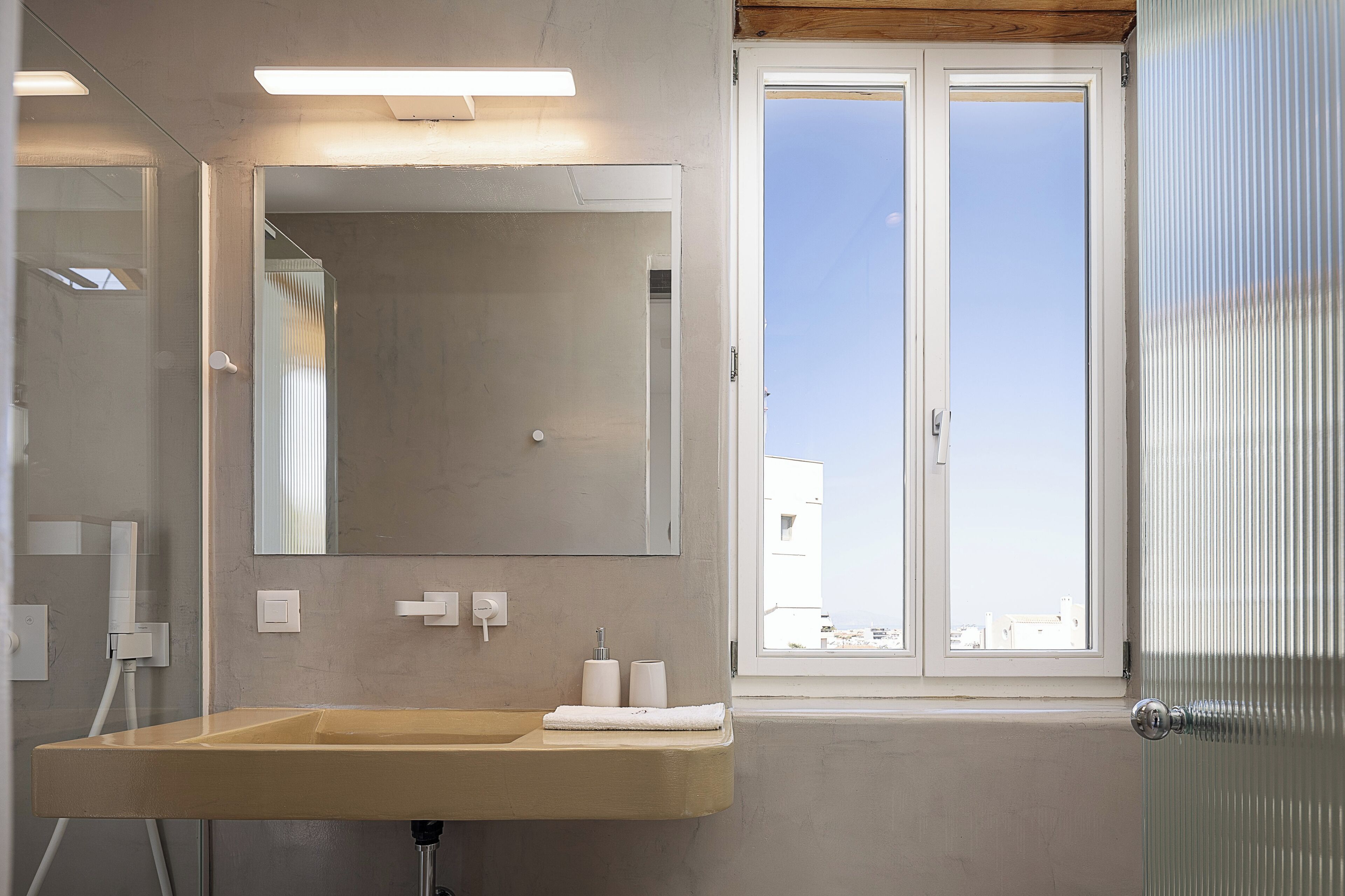 Ein modernes Badezimmer mit einem großen Spiegel, einem Waschbecken und einem Fenster mit Blick auf Gebäude.