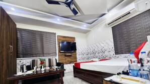 A modern hotel room with a bed, a TV, a wooden wardrobe, a sofa, and a small table with a vase and a plant. - Anandaloke Residency (Kolkata)