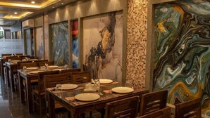 A restaurant with wooden tables and chairs, large abstract paintings on the walls, and a tiled backsplash. - Anandaloke Residency (Kolkata)