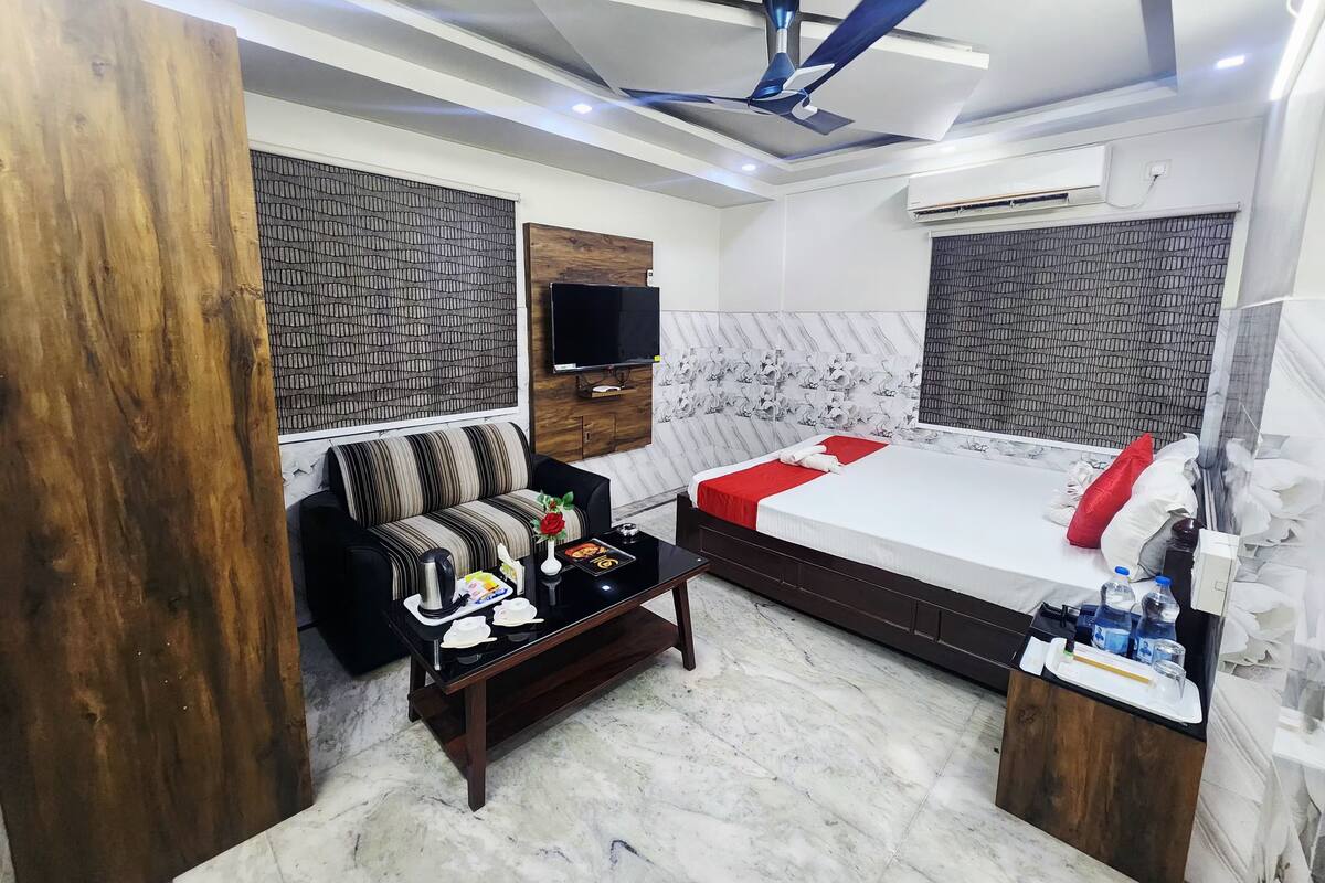 A modern hotel room with a large bed, a sofa, a coffee table, and a TV.