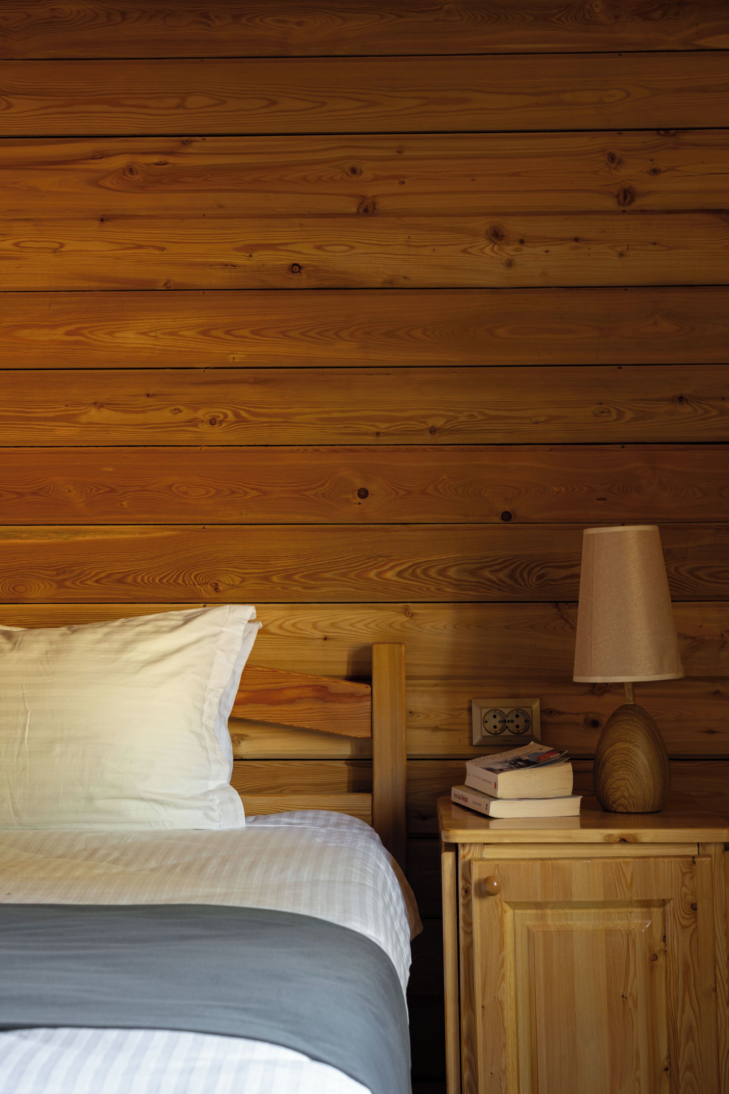 Una habitación con paneles de madera, una cama, una mesita de noche con lámpara y un mueble bajo.