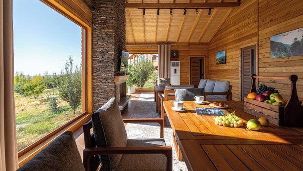 A wooden cabin with a dining area, stone pillar, and a view of the outdoors. - Silver Valley (Kumushkan)