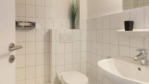 A bathroom with white tiles, a toilet, a sink, a mirror, and a small plant.