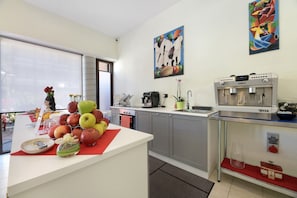 Une cuisine moderne équipée d’une machine à café, d’un présentoir à fruits et agrémentée d’œuvres d’art aux murs.
