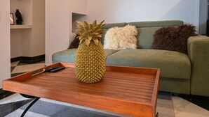 A pineapple on a wooden tray on a coffee table in a living room with a green sofa and a fluffy white pillow. - Unique Vacation Rental in Losone (Losone)