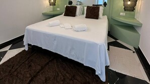 A modern hotel room with a large bed, white linens, two bedside tables with lamps, a large mirror, and a black and white checkered floor. - Unique Vacation Rental in Losone (Losone)