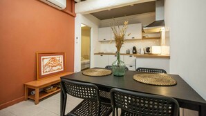 Un comedor con una mesa negra, cuatro sillas, un florero con plantas secas y un cuadro en la pared.