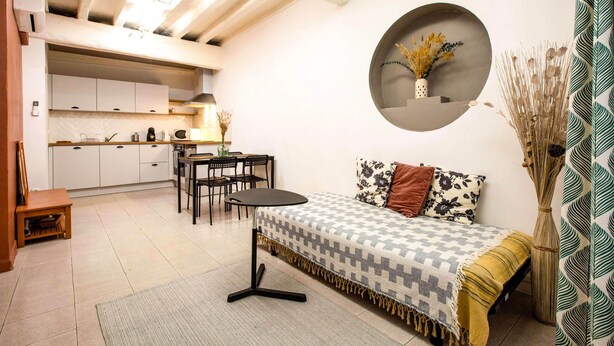 Un espacio habitable compacto con kitchenette, comedor y sofá con un cojín estampado.