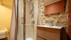 Un baño con cabina de ducha de vidrio, tocador de madera con lavamanos y pared de piedra.