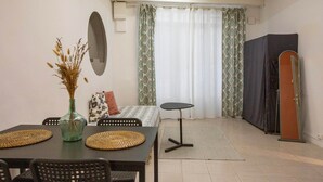 Un comedor con una mesa, sillas, un florero con plantas secas, un espejo y una cama con cortinas estampadas.