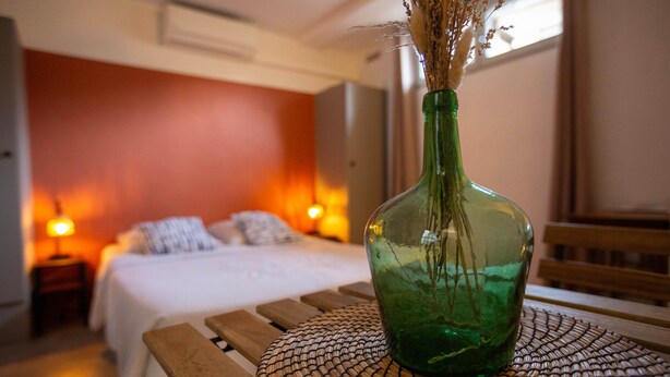 A bed with white linens, a green vase with dried flowers, and a woven placemat on a wooden table. - ✯ RENOVATED ✯ Charming studio Palais des Papes (Avignon)