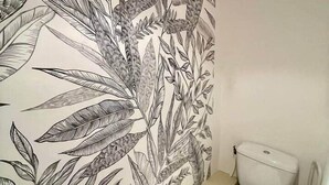 A bathroom with a toilet, a bidet, and a wall with a botanical mural.