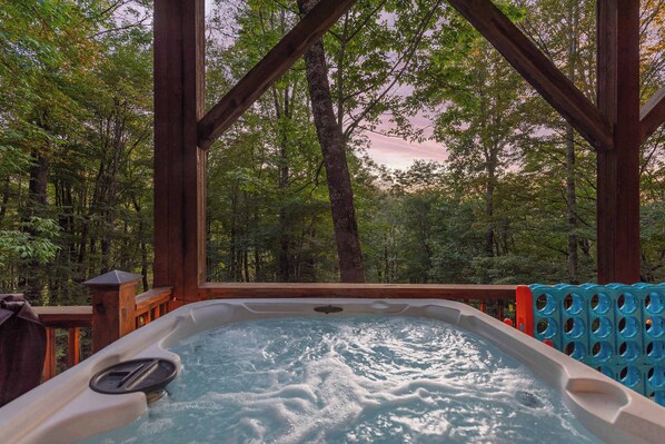 A hot tub with a wooden deck and a view of a forest.