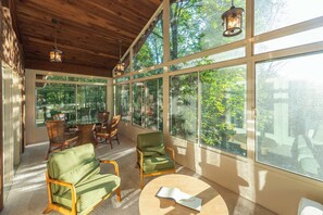 A sunlit room with large windows, a round table, and green chairs.