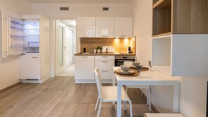 Une cuisine moderne avec des meubles blancs, un plan de travail en bois et un coin repas comprenant une table et des chaises blanches.