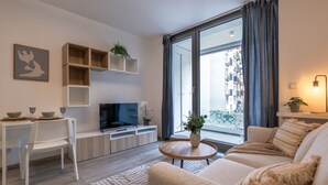Un salon moderne avec un canapé, un téléviseur, une table à manger et un balcon offrant une vue agréable.