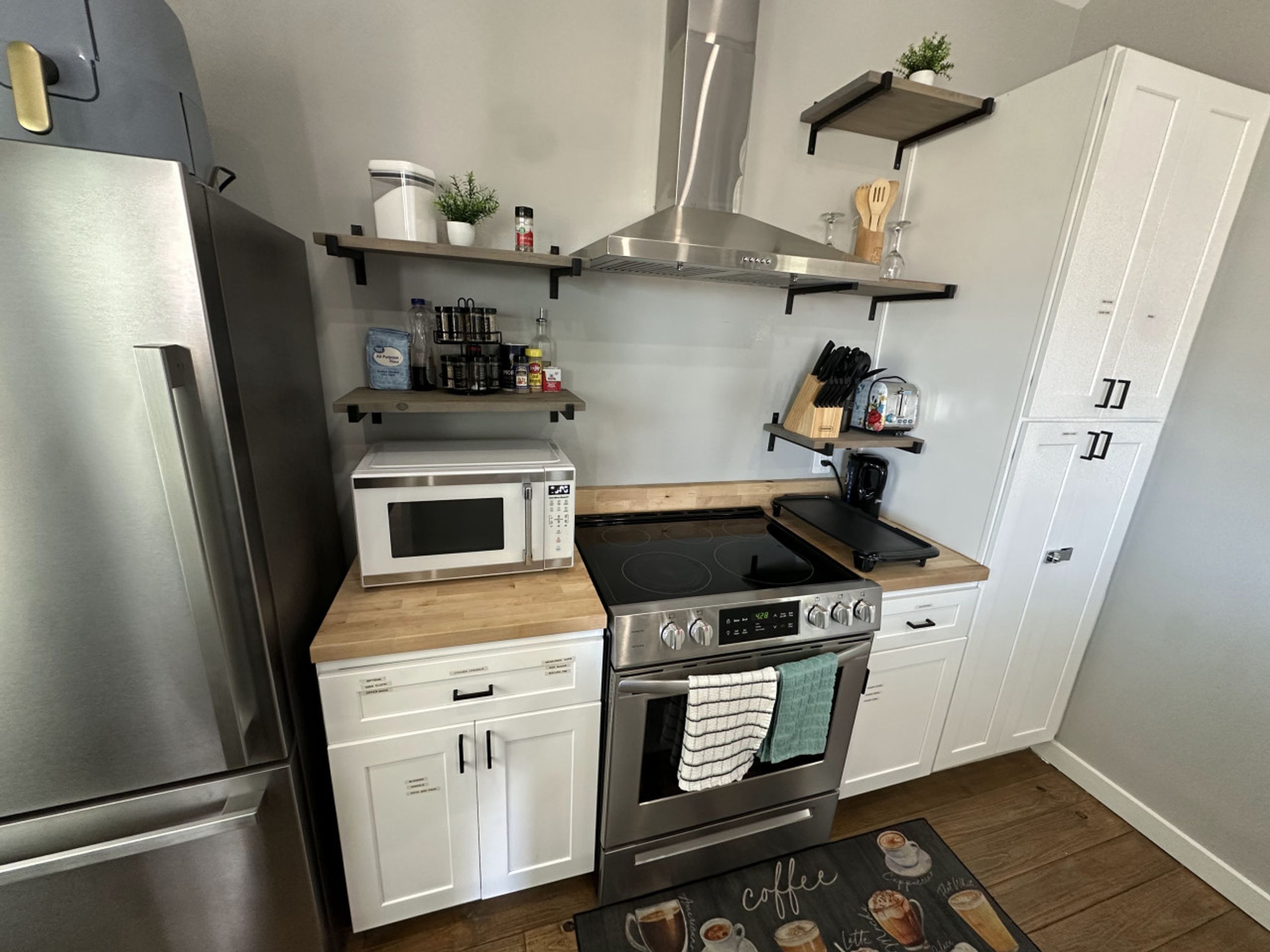 A modern kitchen with a stainless steel refrigerator, a microwave, an oven, and a stove. There are wooden cabinets, a countertop, and a backsplash.