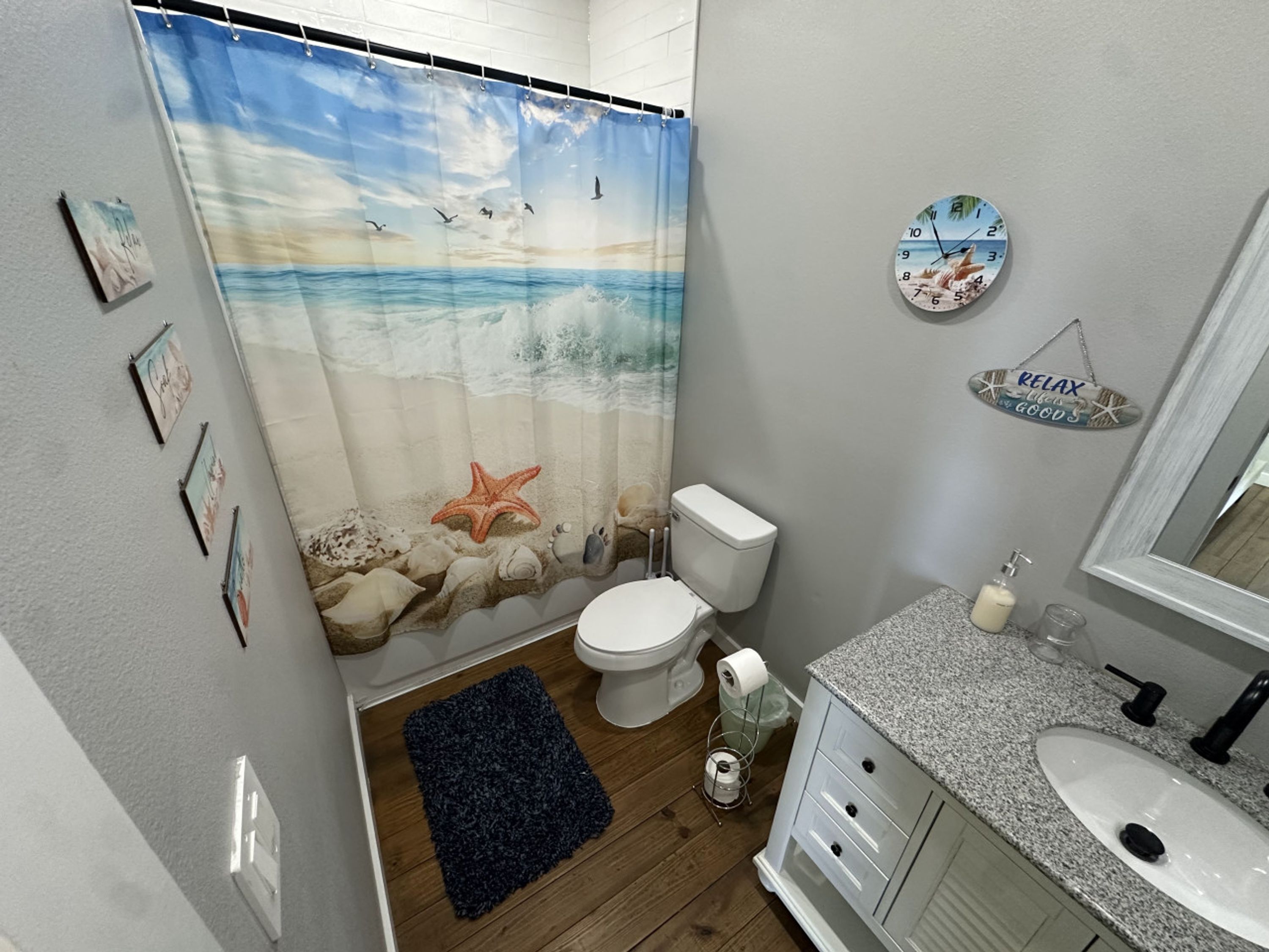 A bathroom with a beach-themed shower curtain, a toilet, a sink, and a mirror.