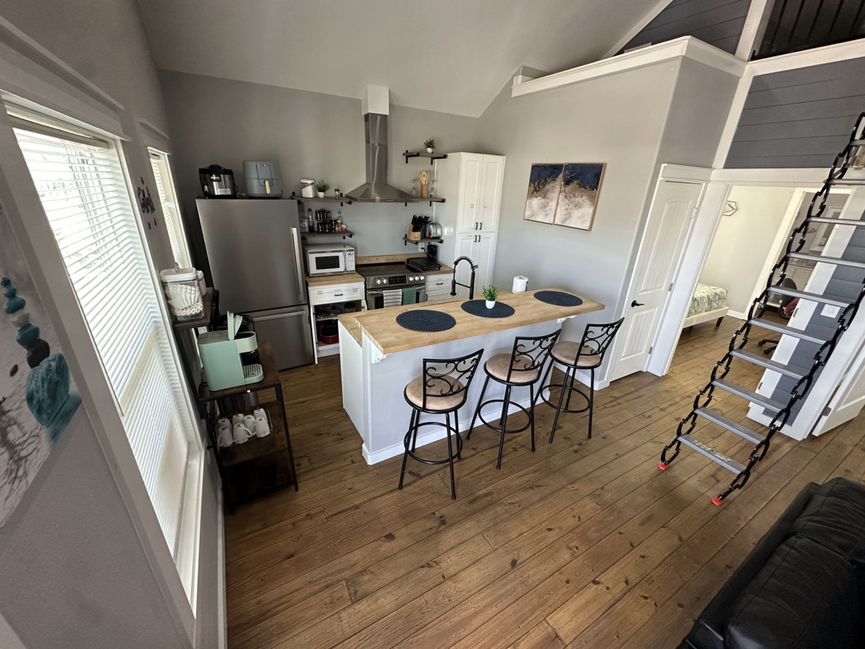 A compact kitchen with a central island, a dining area with bar stools, and a staircase leading to an upper level.
