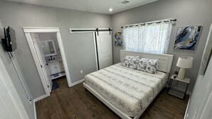 A bedroom with a bed, a walk-in closet, a door leading to another room, and a window with curtains. - Cozy Seaside Cottage Escape (Port Bolivar)