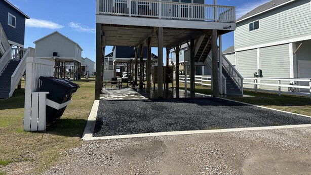 A covered outdoor area with a staircase leading to a balcony, surrounded by houses. - Cozy Seaside Cottage Escape (Port Bolivar)
