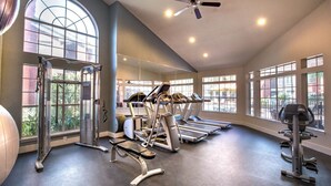 Ein Fitnessraum mit Laufbändern, Kraftgeräten und einem Deckenventilator.