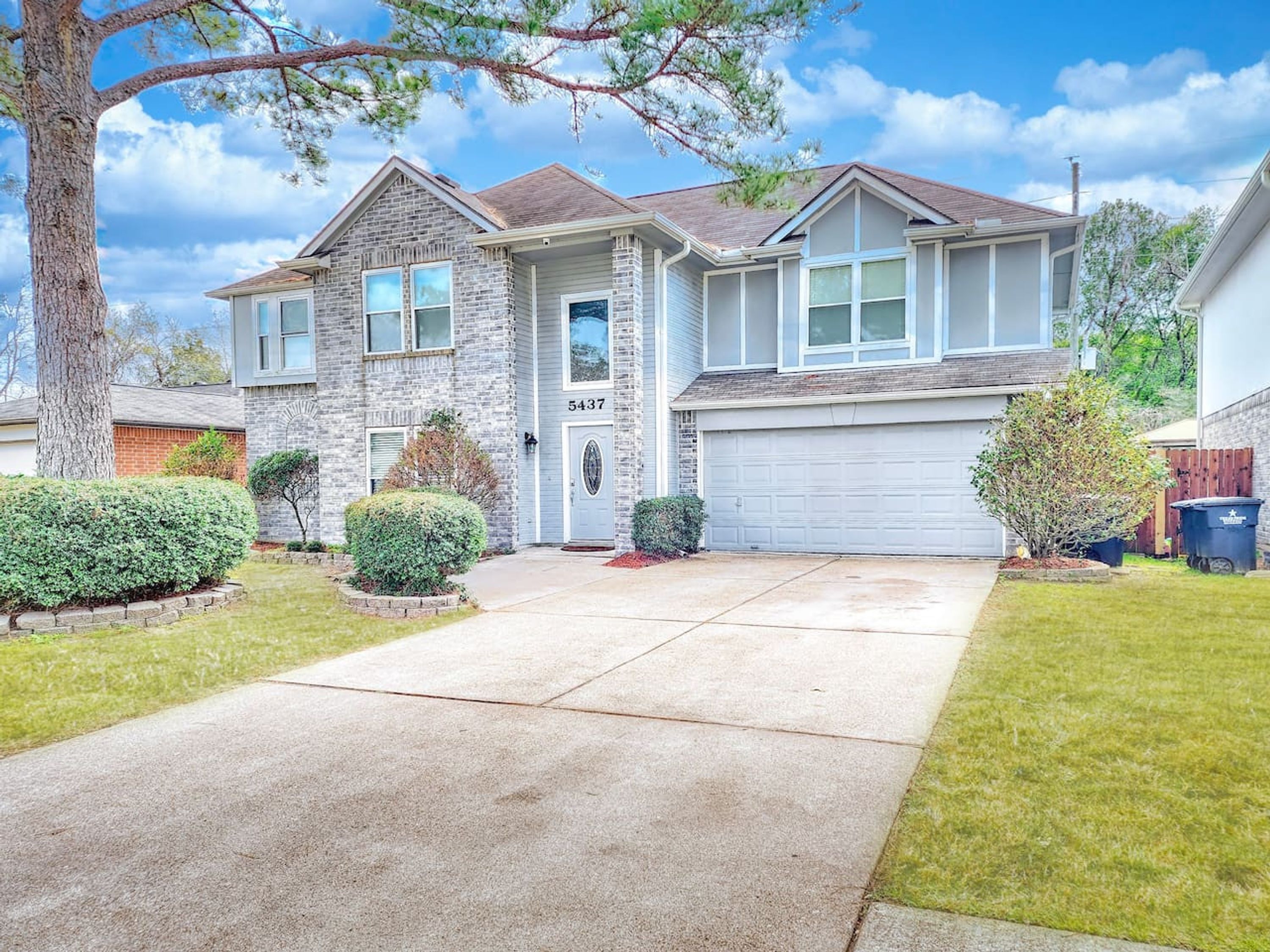 A two-story house with a stone facade, a garage, and a well-maintained lawn.