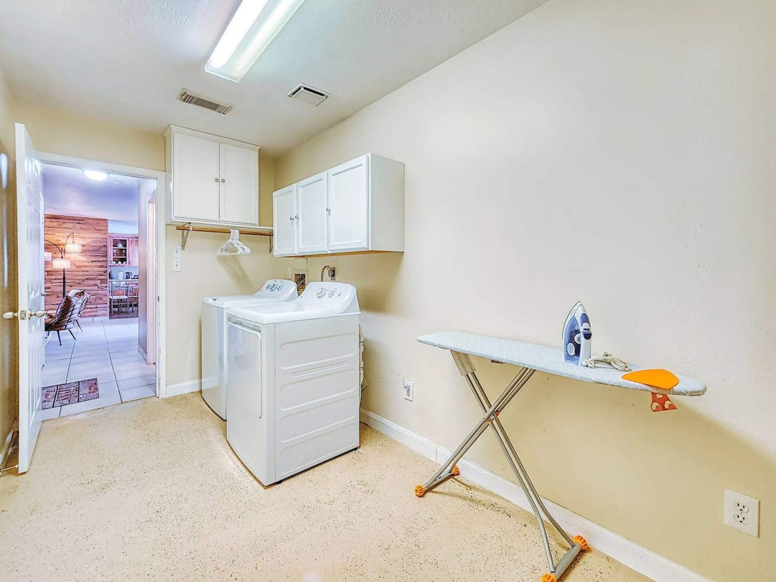 A laundry room with a washing machine, dryer, ironing board, and cabinets.