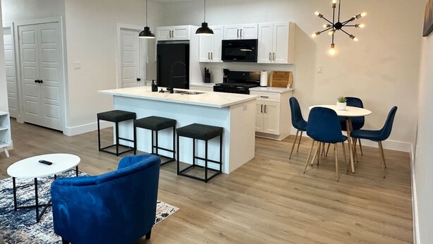 Une cuisine moderne avec des meubles blancs, un réfrigérateur noir et un îlot central doté de tabourets de bar. On y trouve également un coin repas avec des chaises bleues et une petite table.