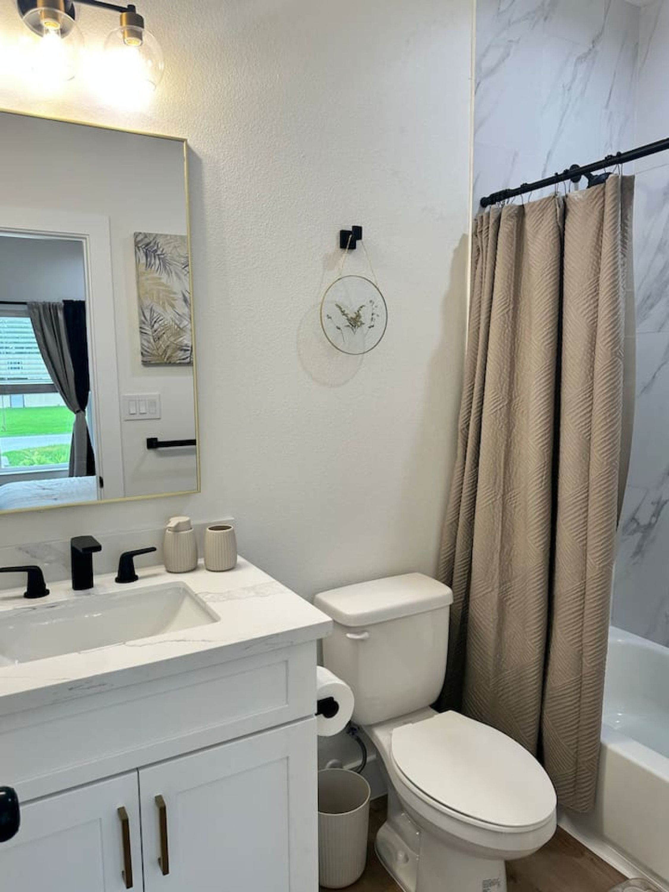 Une salle de bain avec un lavabo blanc, des robinets noirs, des toilettes et un rideau de douche.