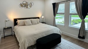 Une chambre à coucher comprenant un lit, une table de chevet, une lampe sur pied, un ventilateur de plafond et une fenêtre avec des rideaux.