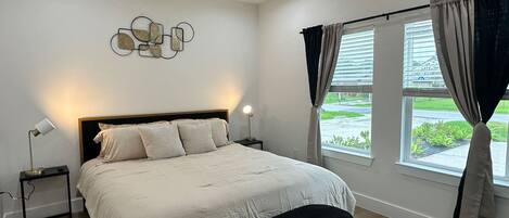 A bedroom with a bed, a nightstand, a floor lamp, a ceiling fan, and a window with curtains.