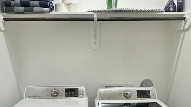 A laundry area with two front-loading washing machines, a shelf with folded towels, a green iron, and two spray bottles. - Quiet 3BR Home Fast Access to IAH Downtown (Houston)